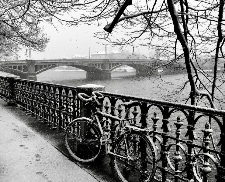 Bicycle covered with snow near bridge in Prague.