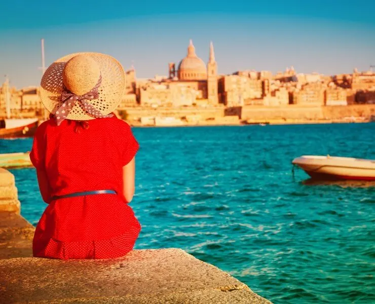 Visiting Malta - lady sitting in sun wearing a hat with Valletta in background