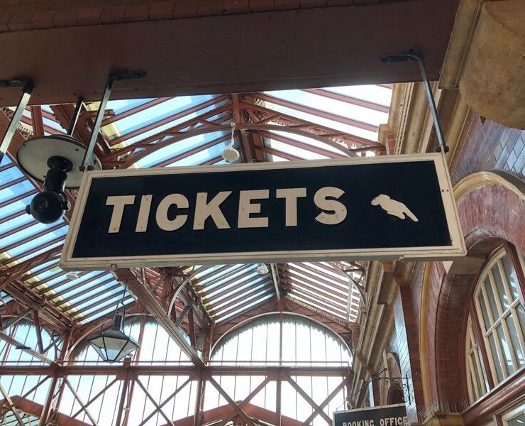 Sign for tickets in a train station in England with a hand pointing to the ticket office