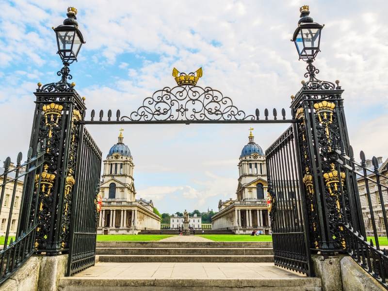 Gates with ornate metalwork in black and gold and old buildings behind which are UNESCO World Heritage Sites in the UK