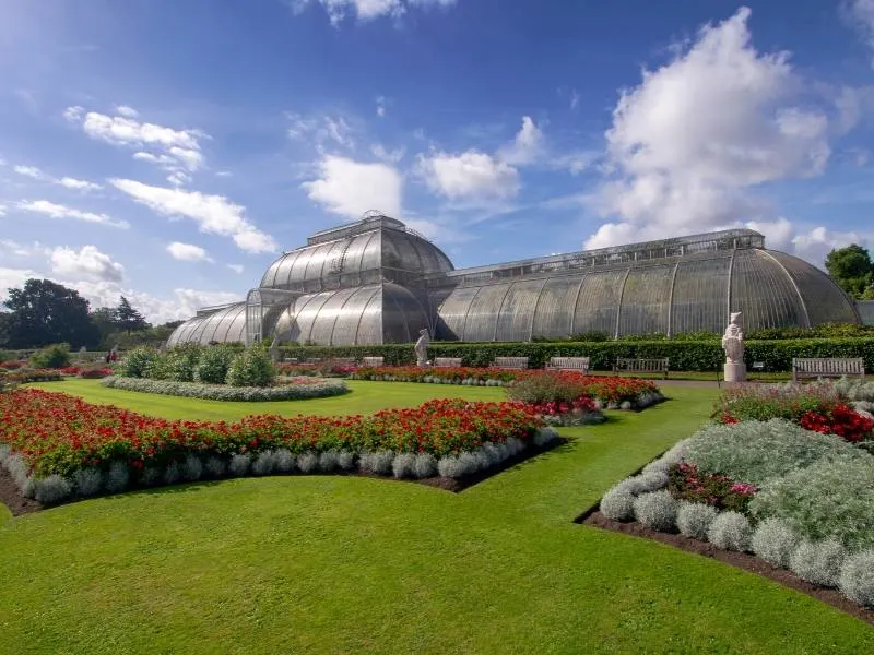 A large palm house surrounded by green lawns and red flowers