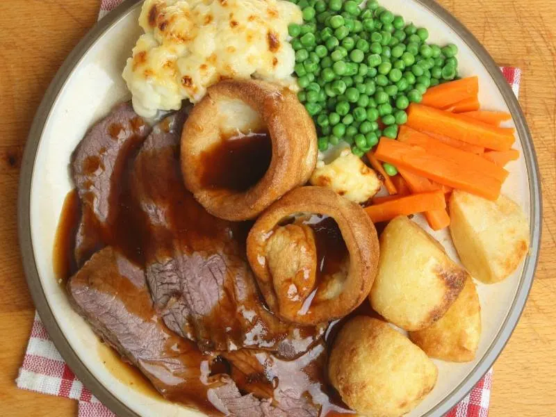 A Roast Dinner with meat, vegetables and Yorkshire Pudding on a white plate