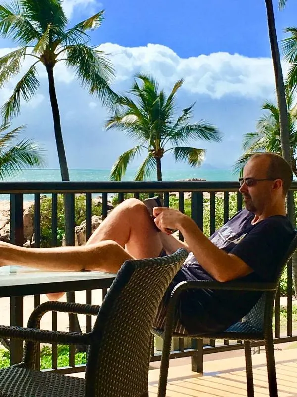 A man relaxing with a book in front of some palm trees and a beach one of the things to do in Bowen