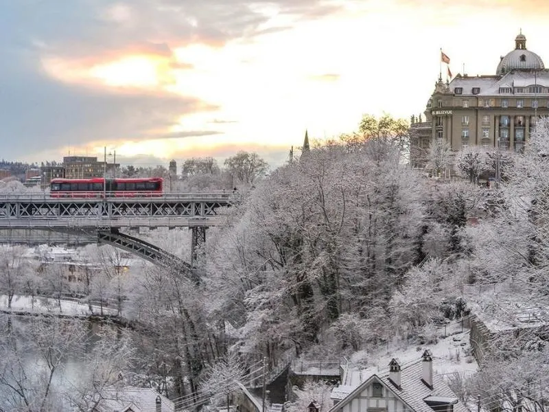 Bern in the winter snow with a red bus crossing a snow covered bridge