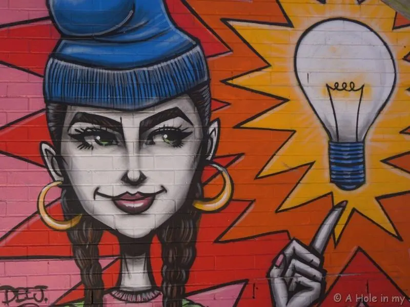 A colourful piece of street art in Perth showing a woman pointing to a light bulb