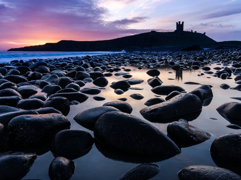 Dunstanburgh Castle in silhouette at sunset