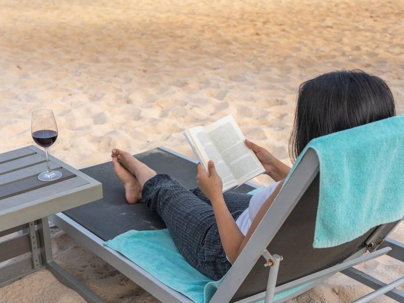 Woman sitting on a beach reading a selection of best books from around the world.