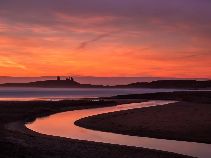Dunstanburgh Castle silhouetted at sunset.