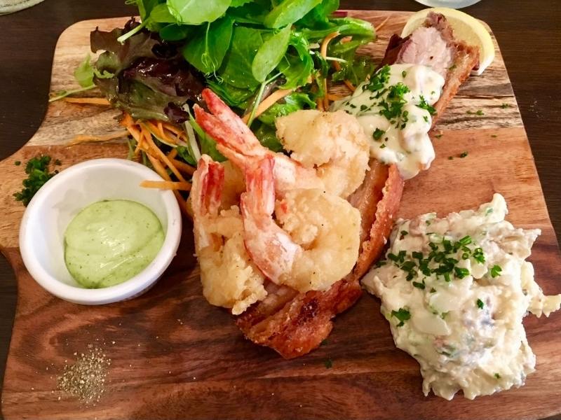 Prawns and pork served on a wooden platter with potatoes.