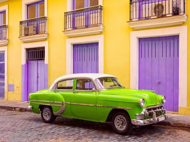 Car in Cuba in front of yellow and purple doors.