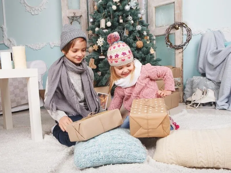A boy and a girl opening their travel gifts for children under a Christmas tree.