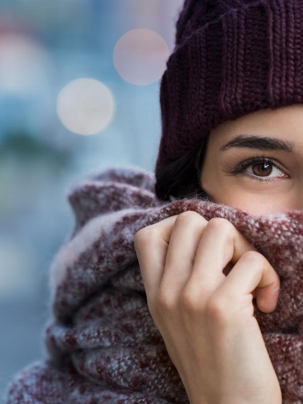 Girl peeking above a scarf with a woolly hat on.