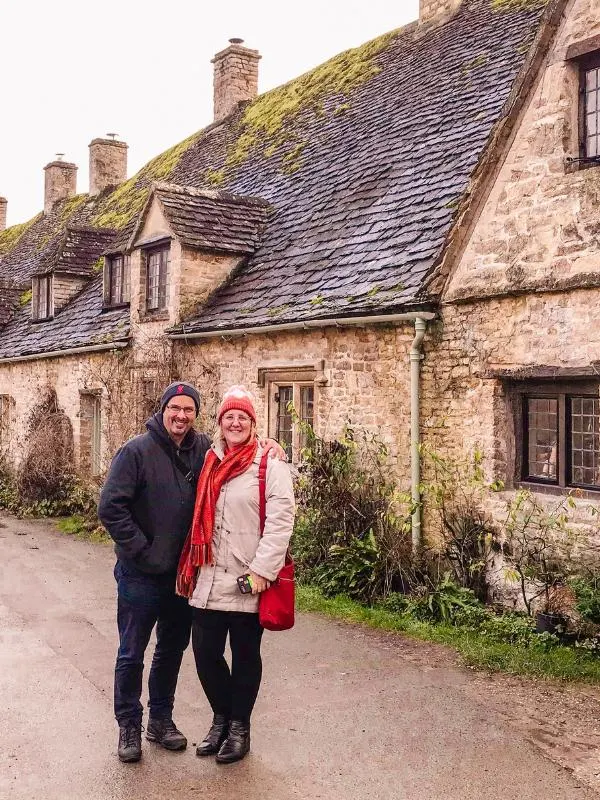 Man and woman standing on front of a row of cottages in winter in the Cotswolds.