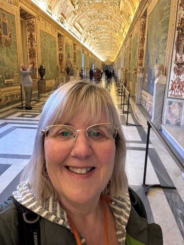 tips for visiting the Vatican - a lady standing in a corridor with paiings on the wall and ceilings.