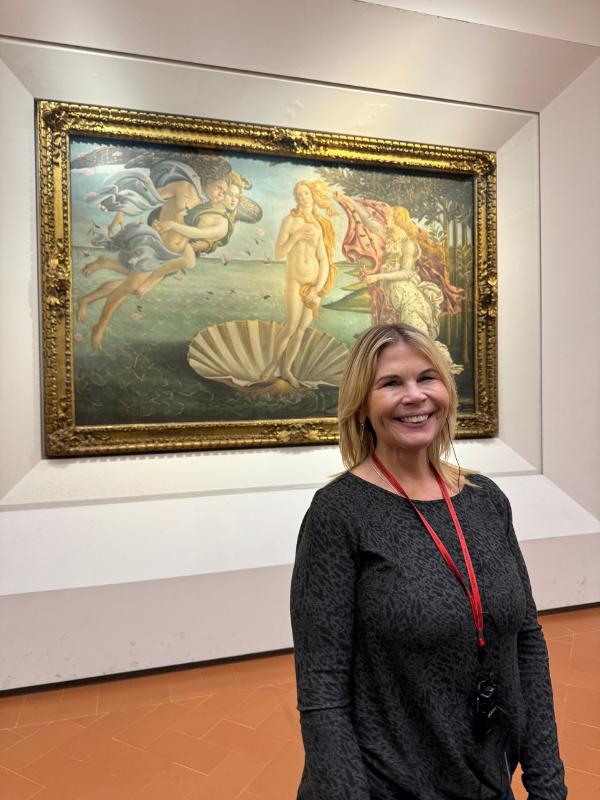 A lady standing in front of the painting the birth of venus.